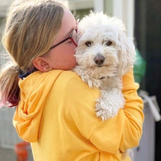 women in yellow sweater kissing fluffy white dog face